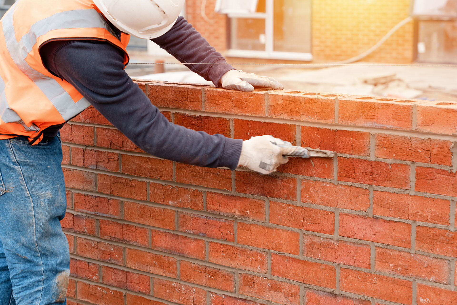 Bricklayer laying bricks on mortar on new residential house construction